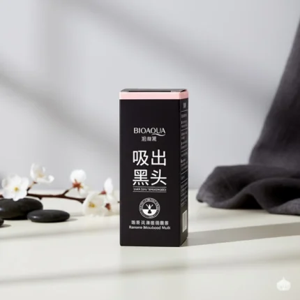 Black and pink box of BIOAQUA Activated Carbon Blackhead Mask, styled with spa stones, white cherry blossoms, and dark grey fabric on a bright surface.