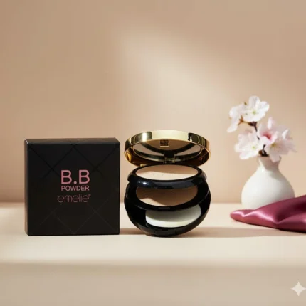 Emelie BB Powder compact with two shades, applicator sponge, black and gold case, next to its packaging, small white vase with pink flowers, and a purple silk cloth on a beige background