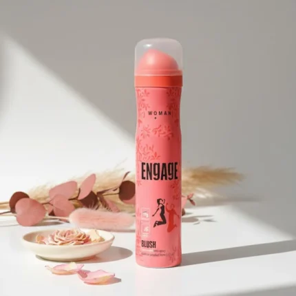 Engage Blush Woman Deodorant Spray. Pink and coral can on a bright, minimal white surface with soft floral and shadow accents.