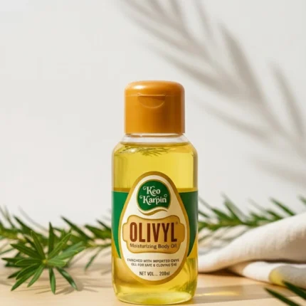 Keo Karpin OLIVYL Moisturizing Body Oil in a 200ml clear bottle with a green and yellow label, sitting on a wooden surface with green foliage and soft shadows.