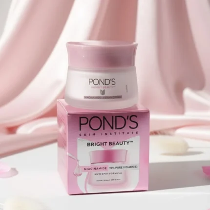Pond's Bright Beauty Face Cream jar (white lid, pink base) on a clean, minimal background with pink floral props and strong natural shadows.