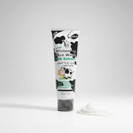 A white and black plastic squeeze tube of "Whitening Face Wash Milk Extract" is shown standing upright on a white surface. A small dollop of the white face wash is squeezed out and placed next to the tube. The packaging features a cartoon cow face with green eyes and a black and white cow print pattern. The text on the tube is in both English and Arabic. The product is labeled "NEW," "Milk," and "Y&G." It is also described as "Deep Cleaning, Moisturizing & pH-Balance" and "NET WT. 190 ml.