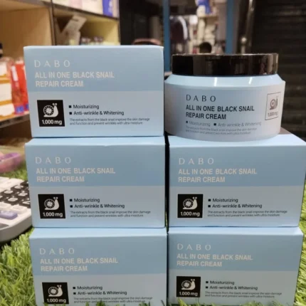 Multiple boxes and a jar of DABO All In One Black Snail Repair Cream arranged on green artificial grass in a shop setting.
